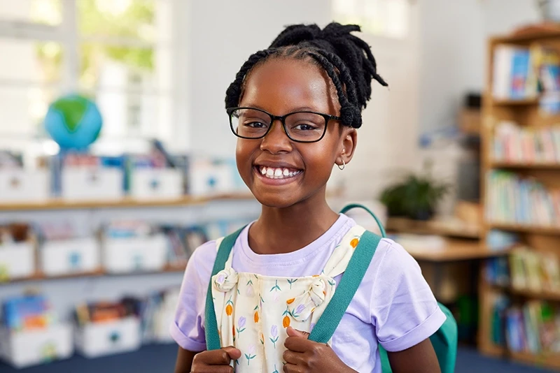 a little girl wearing glasses and smiling in a classroom