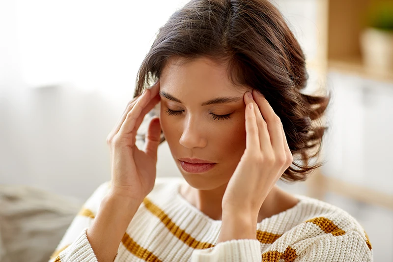 a woman looking uncomfortable and holding her hands to her head